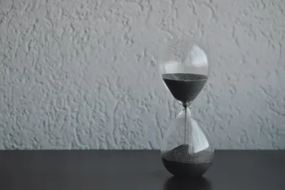 An hourglass with dark sand against a textured wall