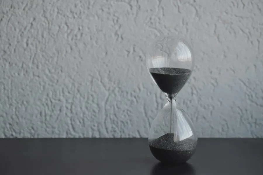 An hourglass with dark sand against a textured wall