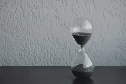 An hourglass with dark sand against a textured wall