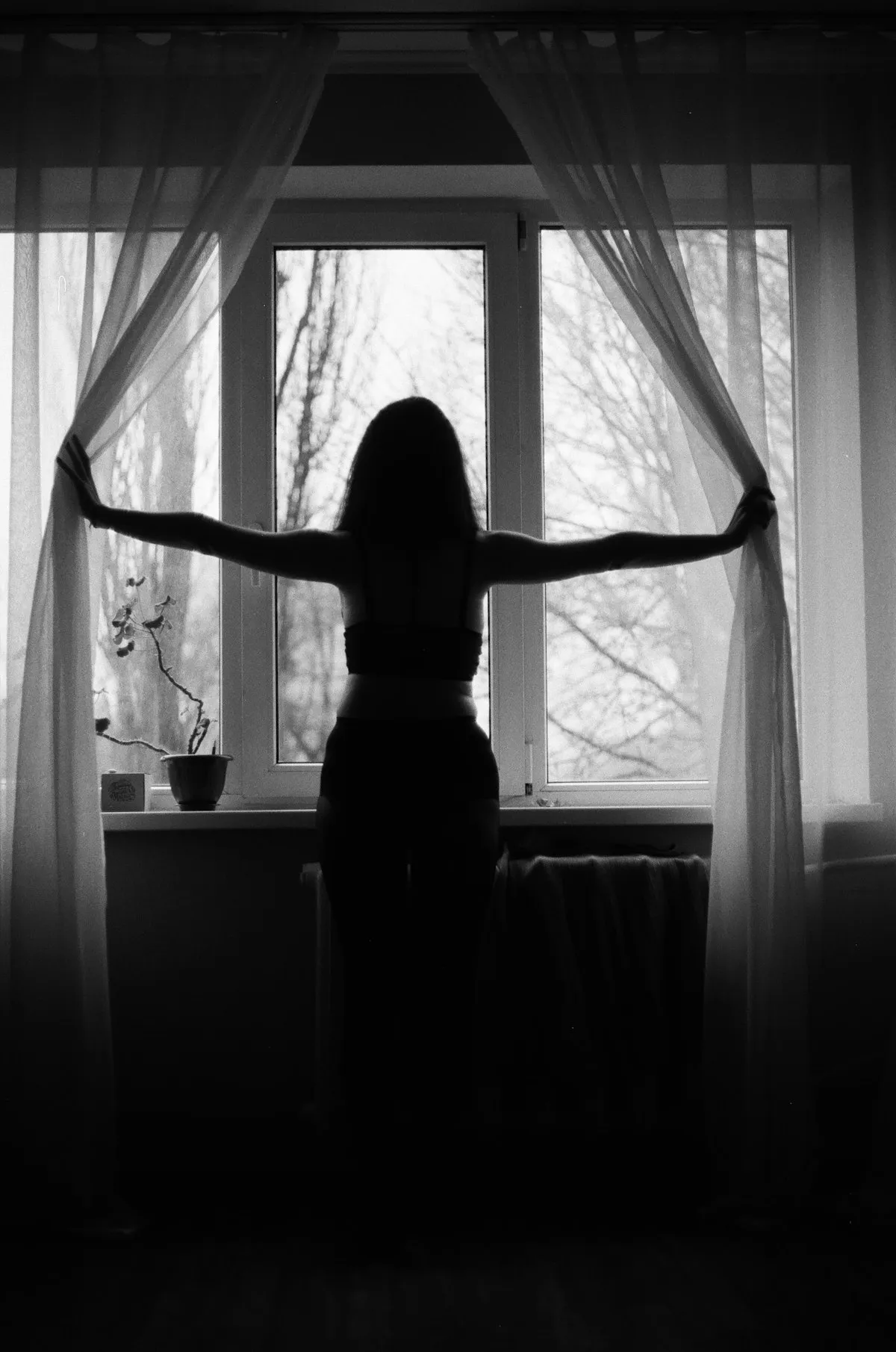 A woman opening curtains to morning light